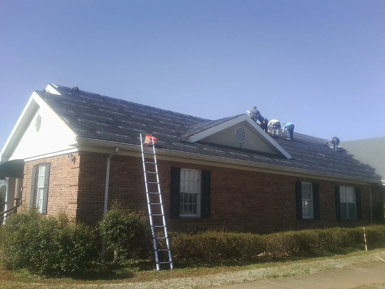 Crew tearing shingles off a brick ranch roof with a ladder set — Emergency Roof Repair work by our crew in Lake Milton