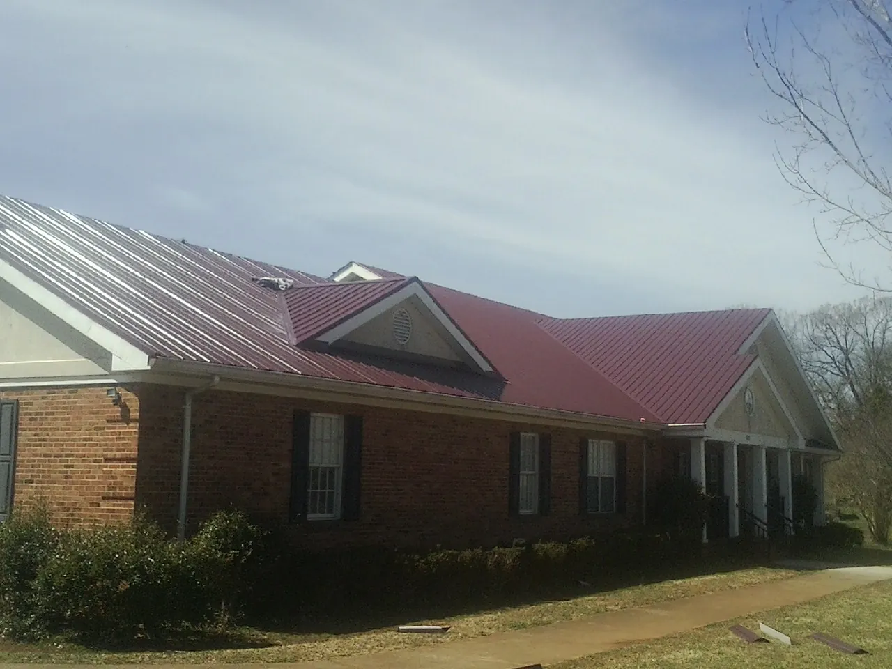 Red metal roof with gabled entries on a long brick building, from a Hail Damage Roof Repair job in Lake Milton