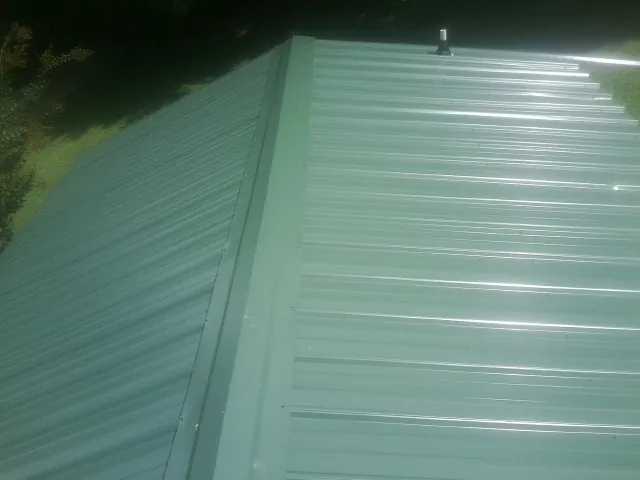 New green metal panels meeting at the ridge of a roof — Flat Roof Repair work by our crew in Lake Milton