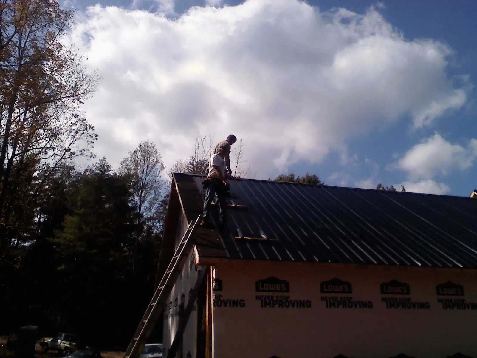 Roofer fastening dark metal panels high against a cloudy sky, from a Roof Inspection job in Lake Milton