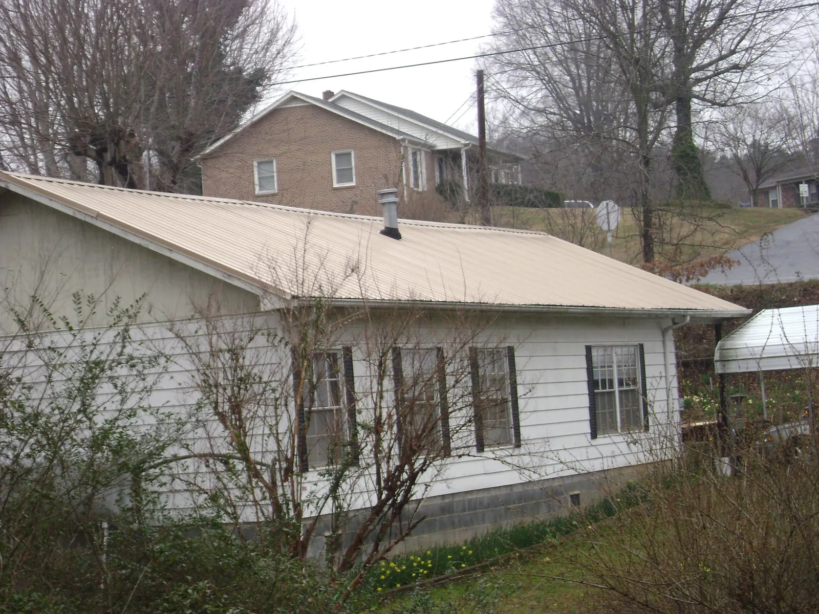 Tan metal roof on a white sided house set into a hillside — Commercial Roofing by Roofing Brothers in Lake Milton