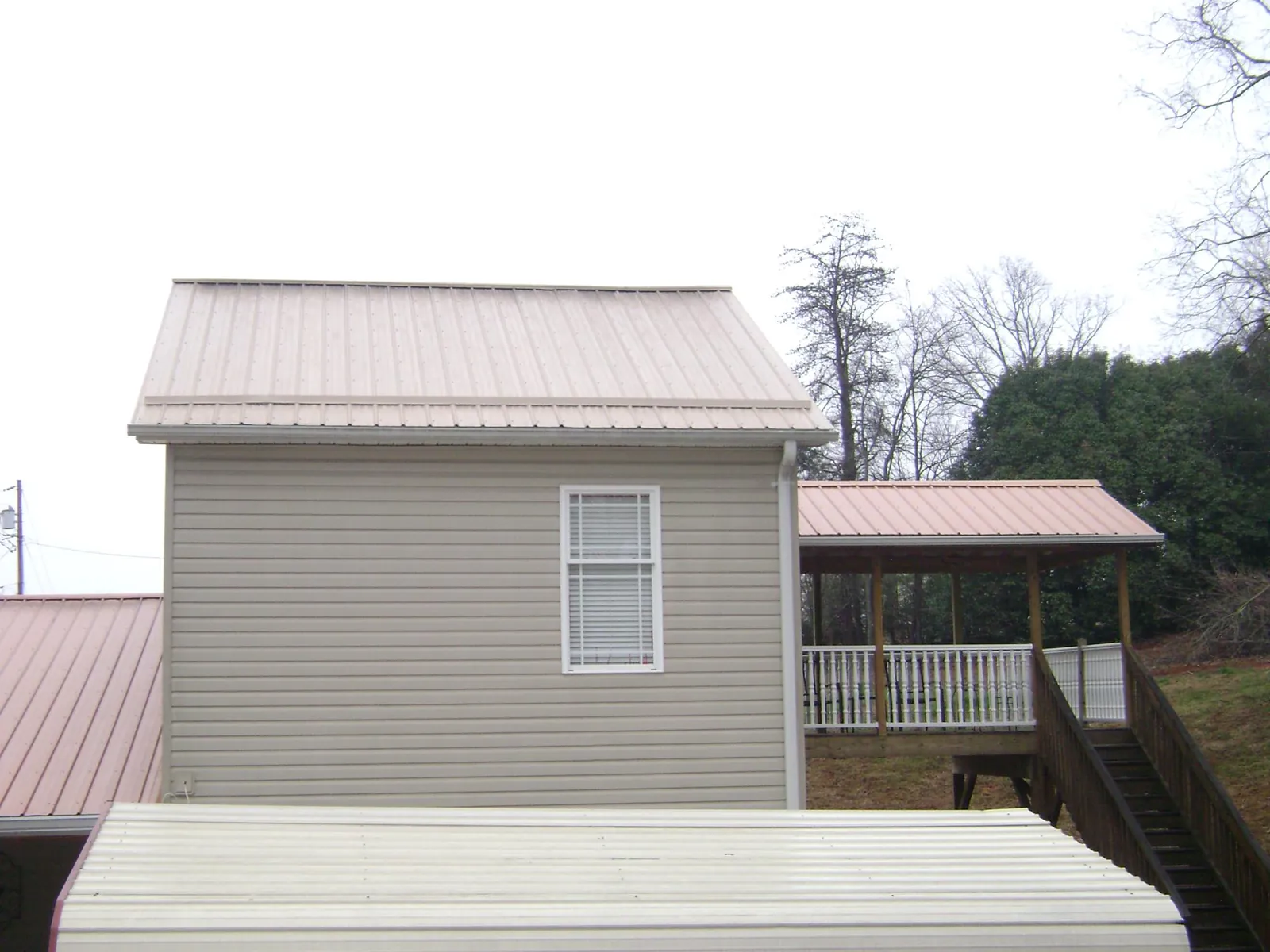 Tan metal roofs on a two story addition and attached porch, from a Roof Replacement job in Lake Milton